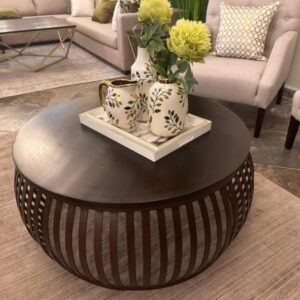 Round wooden drum style coffee table with carved sides placed in a living room setting.